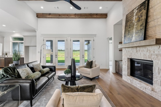 living room with hardwood / wood-style flooring, french doors, beam ceiling, ceiling fan, and a stone fireplace