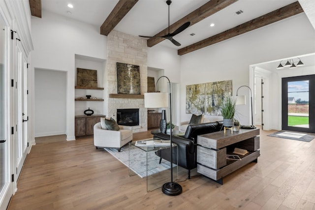 living room with light hardwood / wood-style floors, ceiling fan, a stone fireplace, and beamed ceiling