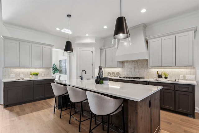 kitchen featuring sink, an island with sink, custom range hood, and a kitchen bar