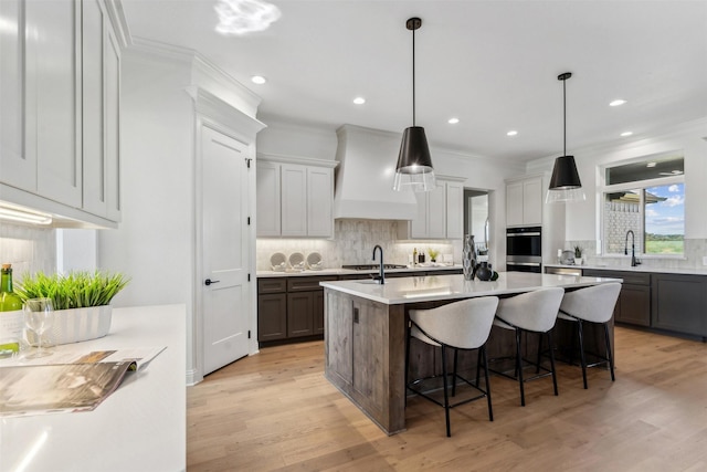 kitchen with a kitchen breakfast bar, custom exhaust hood, a kitchen island with sink, hanging light fixtures, and decorative backsplash