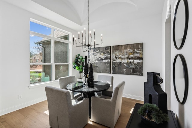 dining space with hardwood / wood-style floors, vaulted ceiling, and an inviting chandelier