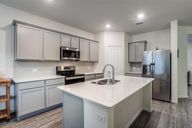 kitchen featuring a kitchen island with sink, appliances with stainless steel finishes, hardwood / wood-style flooring, sink, and tasteful backsplash