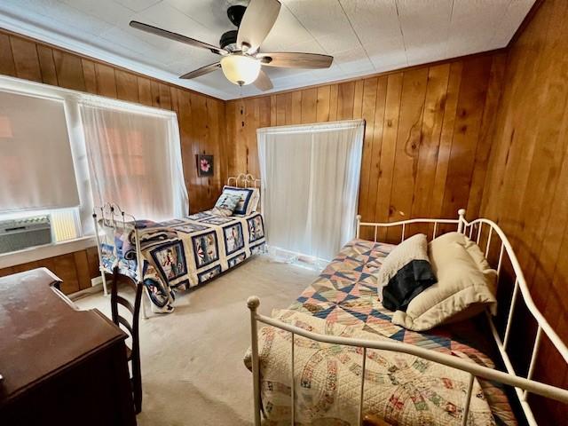 bedroom featuring ceiling fan, light colored carpet, cooling unit, and wood walls