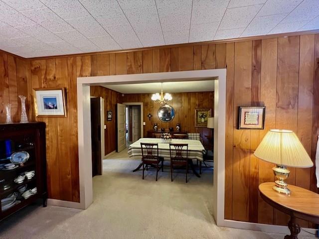 dining space featuring a chandelier, light carpet, and wood walls