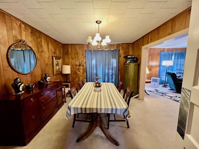 dining space featuring wooden walls, a notable chandelier, and light colored carpet