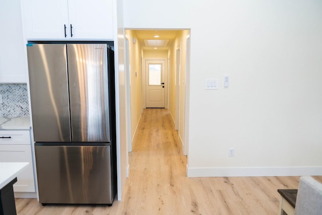 kitchen featuring white cabinetry, backsplash, light hardwood / wood-style flooring, and stainless steel refrigerator