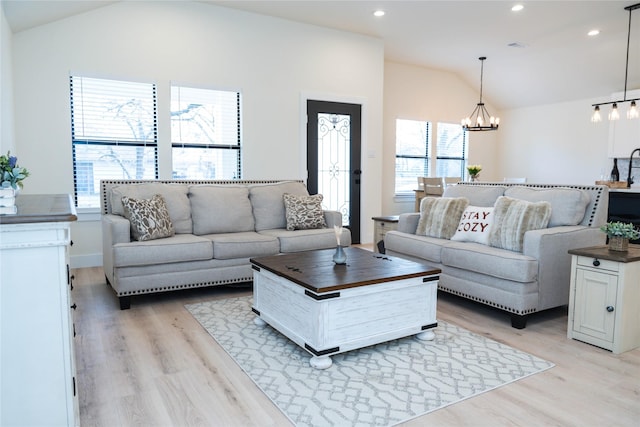 living room with light hardwood / wood-style flooring, a notable chandelier, and vaulted ceiling