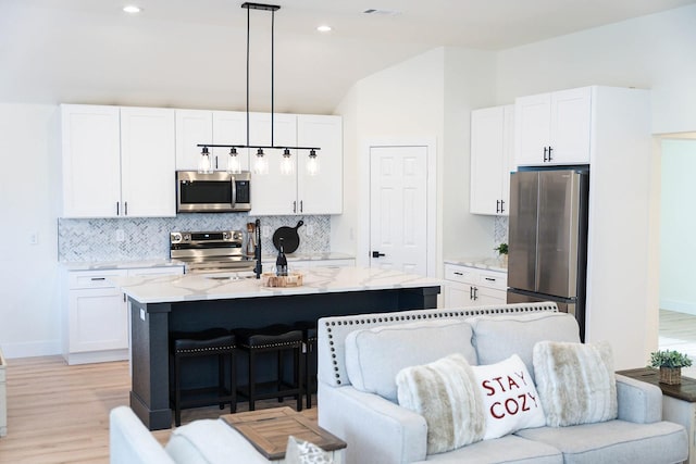 kitchen featuring pendant lighting, stainless steel appliances, an island with sink, and white cabinets