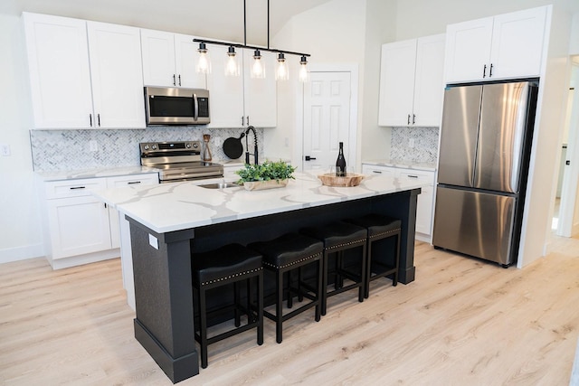 kitchen with light stone counters, a breakfast bar, white cabinetry, light wood-style floors, and appliances with stainless steel finishes