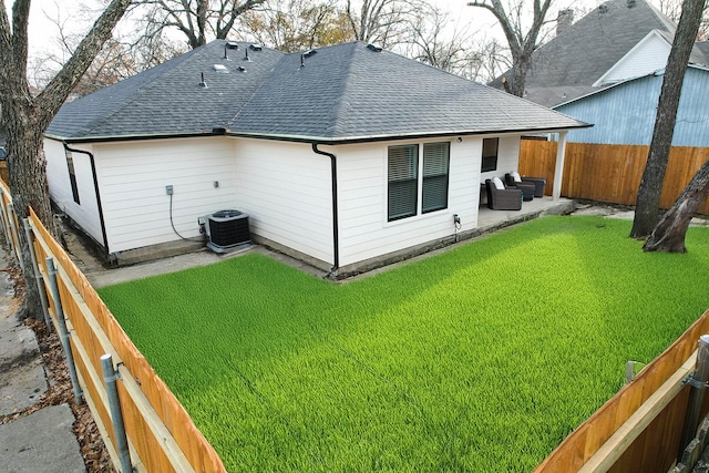 rear view of house featuring a patio, roof with shingles, a fenced backyard, and a lawn