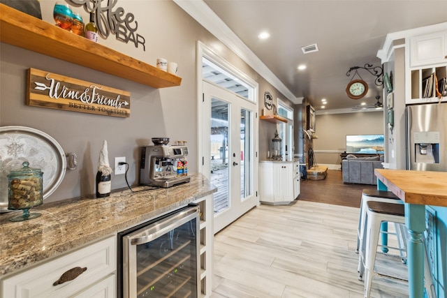 kitchen featuring white cabinets, light stone counters, beverage cooler, stainless steel refrigerator with ice dispenser, and crown molding