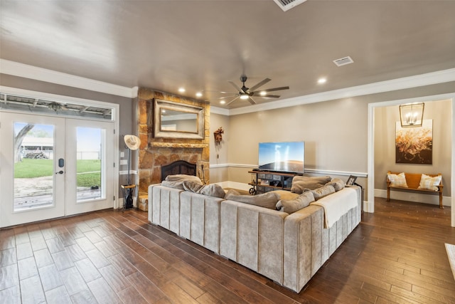 living room with a stone fireplace, french doors, ornamental molding, ceiling fan with notable chandelier, and dark wood-type flooring