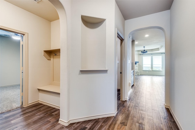 hall featuring dark wood-type flooring, arched walkways, and baseboards