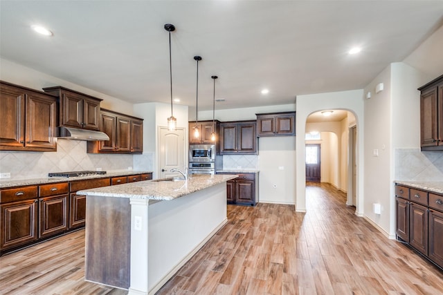 kitchen with sink, decorative light fixtures, light stone counters, an island with sink, and appliances with stainless steel finishes