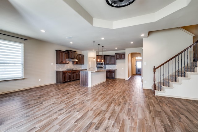 kitchen featuring decorative light fixtures, dark brown cabinetry, a center island with sink, a tray ceiling, and appliances with stainless steel finishes