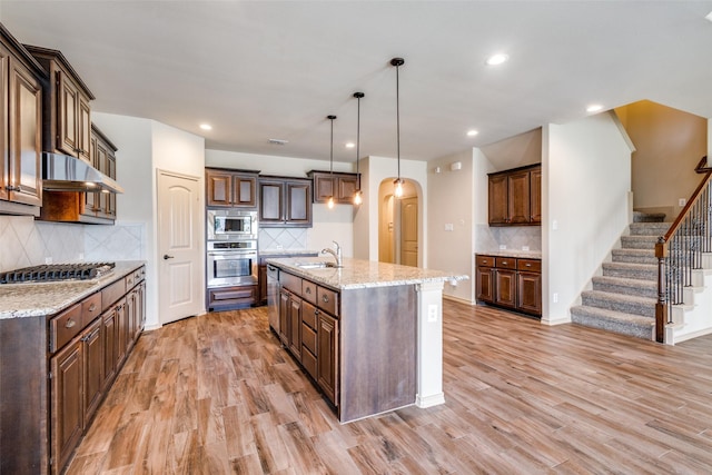 kitchen with decorative light fixtures, stainless steel appliances, tasteful backsplash, a kitchen island with sink, and sink