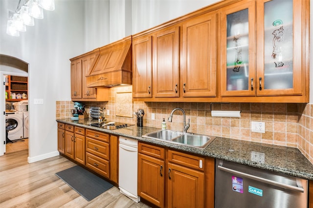 kitchen with washing machine and dryer, dark stone countertops, sink, stainless steel dishwasher, and black electric cooktop