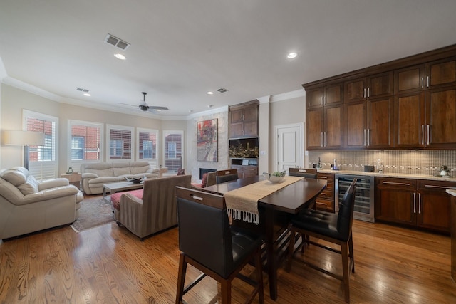 dining space featuring light hardwood / wood-style floors, ceiling fan, ornamental molding, and wine cooler