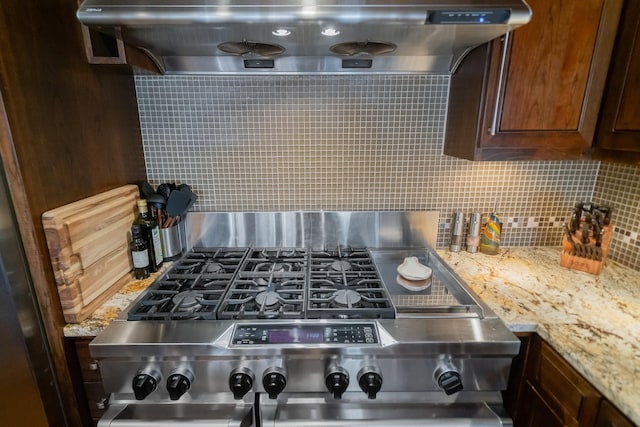 interior details featuring ventilation hood, light stone counters, stove, and tasteful backsplash