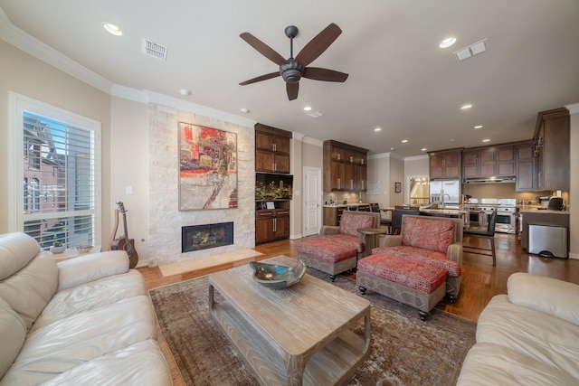 living room featuring dark hardwood / wood-style flooring, a stone fireplace, sink, ornamental molding, and ceiling fan