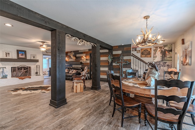 dining space with ceiling fan with notable chandelier, hardwood / wood-style flooring, and a fireplace