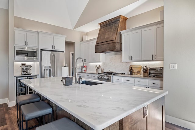 kitchen featuring sink, vaulted ceiling, custom range hood, high end appliances, and a kitchen island with sink