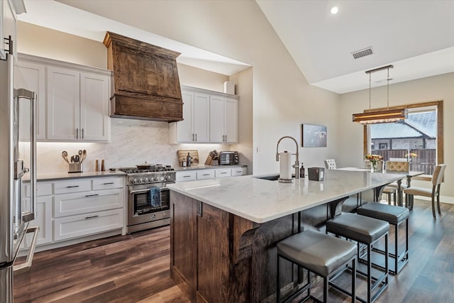 kitchen with decorative light fixtures, vaulted ceiling, a center island with sink, dark hardwood / wood-style flooring, and premium appliances