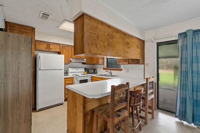 kitchen with white appliances, a breakfast bar area, kitchen peninsula, a textured ceiling, and sink