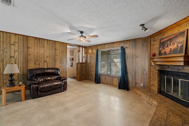 living room featuring wooden walls, a brick fireplace, a textured ceiling, and ceiling fan