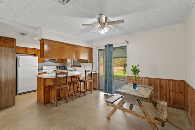 kitchen with white appliances, kitchen peninsula, ceiling fan, wooden walls, and a textured ceiling