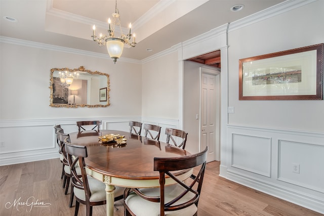 dining space featuring light hardwood / wood-style floors, crown molding, a raised ceiling, and an inviting chandelier