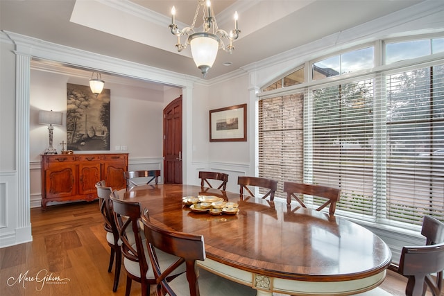 dining area with wood-type flooring, a raised ceiling, crown molding, and a healthy amount of sunlight