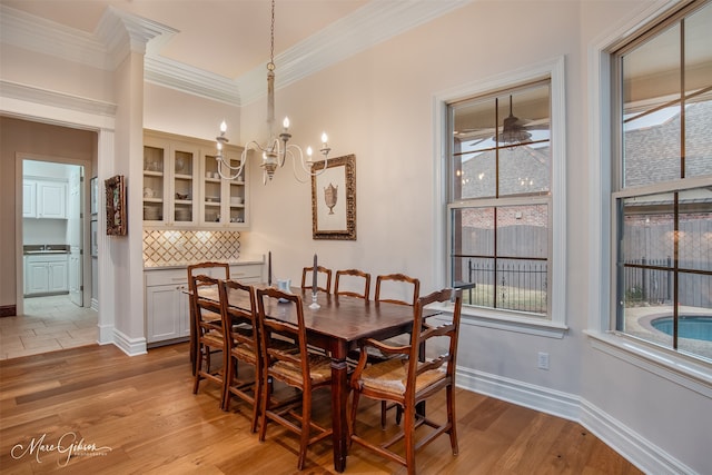 dining area with light wood-type flooring, sink, ceiling fan with notable chandelier, and ornamental molding