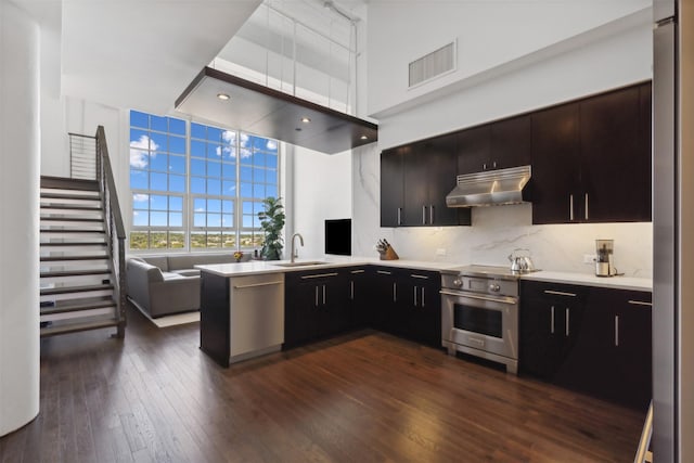 kitchen featuring kitchen peninsula, dark wood-type flooring, tasteful backsplash, appliances with stainless steel finishes, and sink