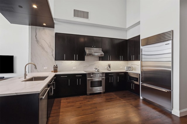 kitchen featuring built in appliances, kitchen peninsula, dark wood-type flooring, light stone countertops, and sink