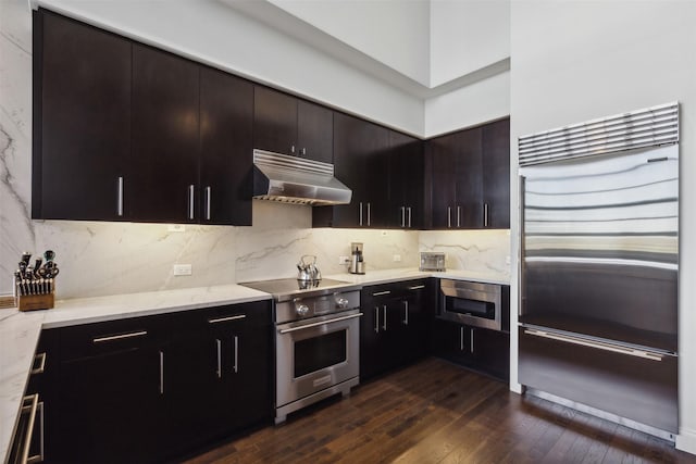 kitchen featuring ventilation hood, dark hardwood / wood-style flooring, decorative backsplash, dark brown cabinetry, and premium appliances