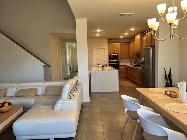 kitchen with appliances with stainless steel finishes, pendant lighting, dark tile patterned floors, decorative backsplash, and an inviting chandelier