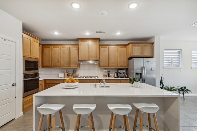 kitchen with appliances with stainless steel finishes, a kitchen breakfast bar, an island with sink, and light tile patterned floors