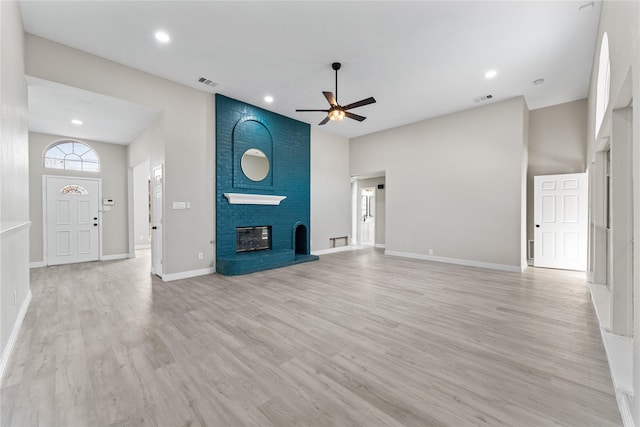 unfurnished living room with ceiling fan, light hardwood / wood-style floors, a brick fireplace, and a high ceiling