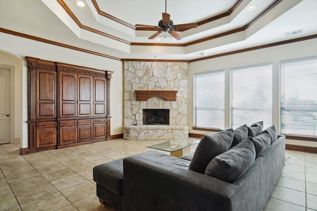 living room with light tile patterned floors, a stone fireplace, crown molding, and a tray ceiling