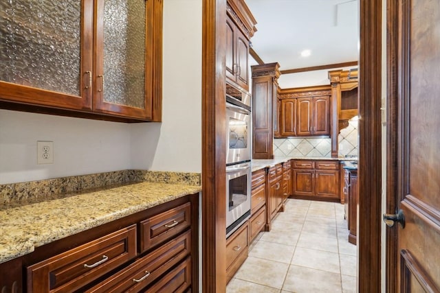 kitchen featuring light stone counters, ornamental molding, light tile patterned floors, decorative backsplash, and stainless steel double oven