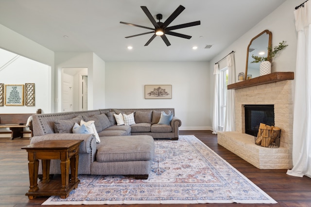 living room featuring dark hardwood / wood-style flooring, a brick fireplace, and ceiling fan