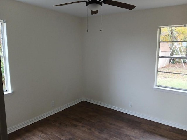 empty room featuring dark wood-type flooring, a ceiling fan, and baseboards