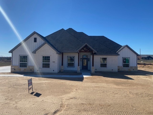 view of front of property featuring stone siding, board and batten siding, and roof with shingles