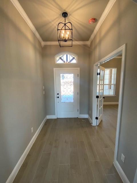 doorway with ornamental molding, an inviting chandelier, wood finished floors, and baseboards