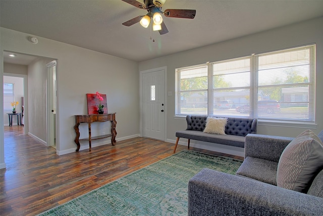 living room featuring dark wood-type flooring, ceiling fan, and a wealth of natural light