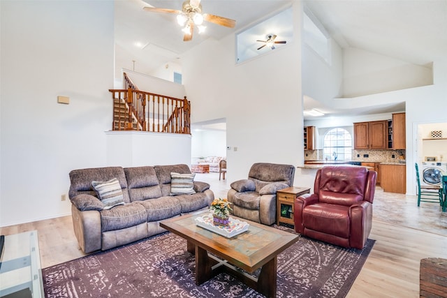 living room featuring washer / dryer, light hardwood / wood-style flooring, high vaulted ceiling, and ceiling fan