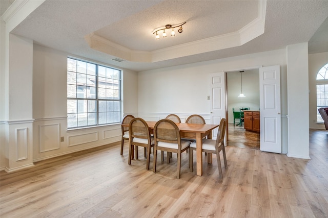 dining room featuring light hardwood / wood-style flooring, a wealth of natural light, a raised ceiling, and a textured ceiling