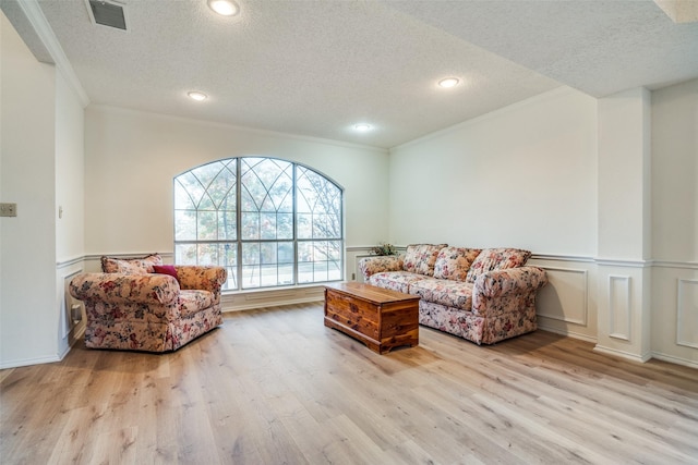 living room featuring ornamental molding, a textured ceiling, and light hardwood / wood-style floors