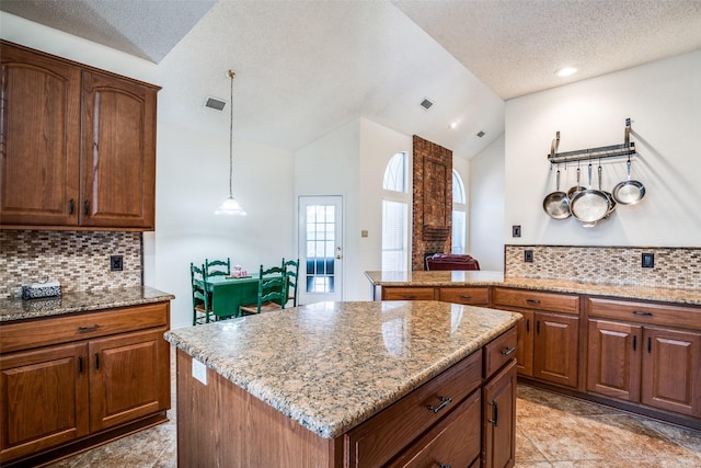 kitchen featuring a kitchen island, pendant lighting, lofted ceiling, decorative backsplash, and light stone counters